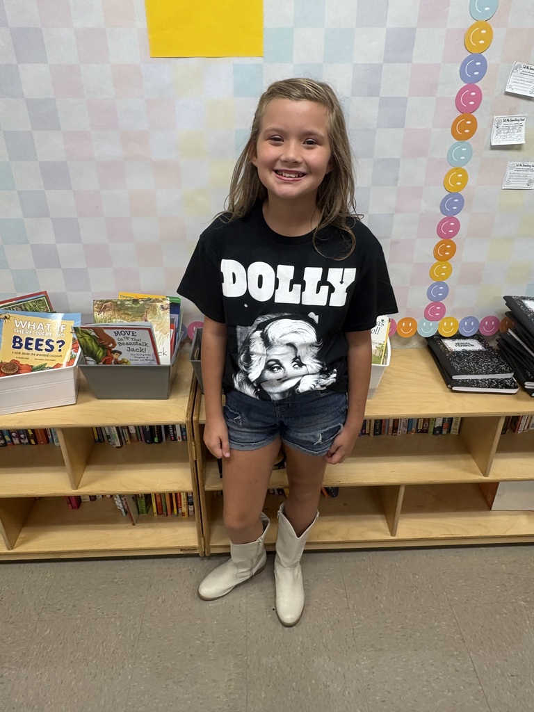 A child in a black T-shirt and white boots stands in a classroom with colorful decorations.