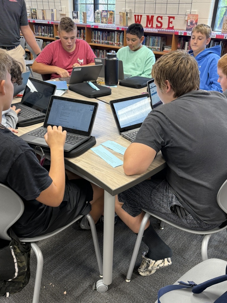 A group of young people sitting around a table in a library. All are working on laptops.