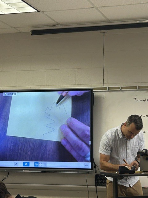 The teacher is demonstrating how to perform reflections, rotations, and translations to her students.