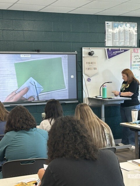 The teacher is demonstrating how to perform reflections, rotations, and translations to her students.