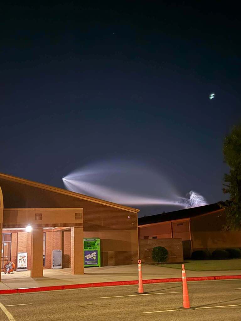 A building entrance at night with smoke rising, a bright moon, and orange traffic cones.