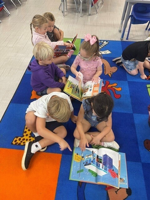 Students reading on the carpet and pointing to the pictures.