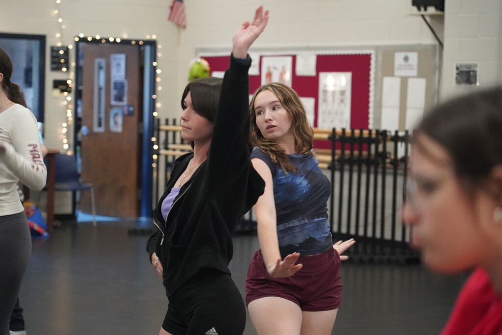 Four women in a dance studio. One woman with her hand raised. One woman in a red shirt.