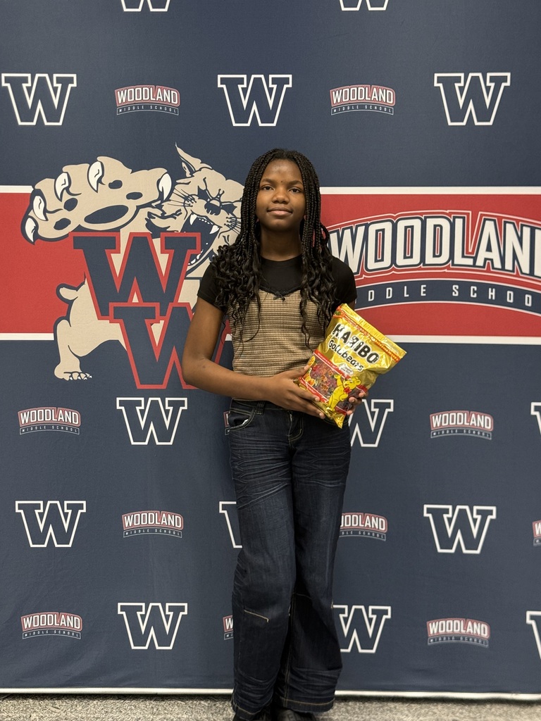 A young girl poses for a photo in front of a Woodland High School banner. She holds a bag of chips.