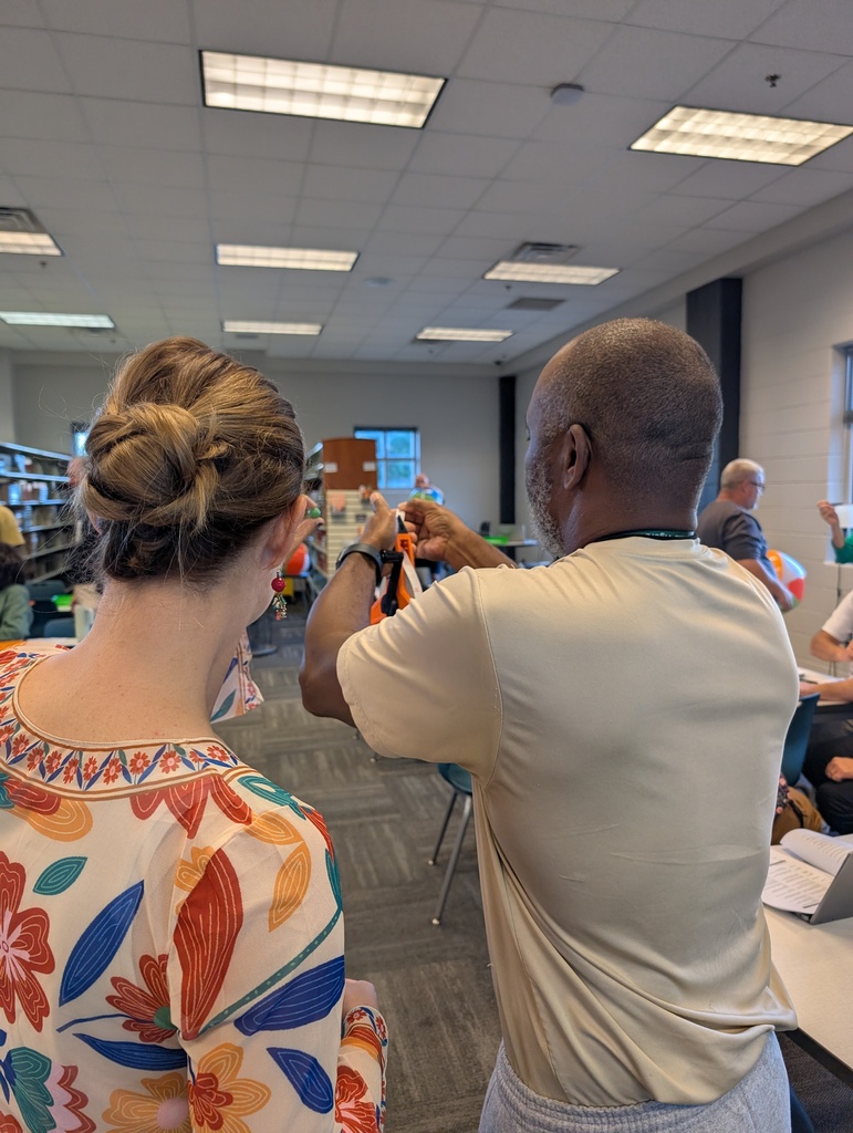 Two teachers stand with a marble and tape measure as they work to determine the distance at which the moon (a marble) blocks out the sun (a beach ball).
