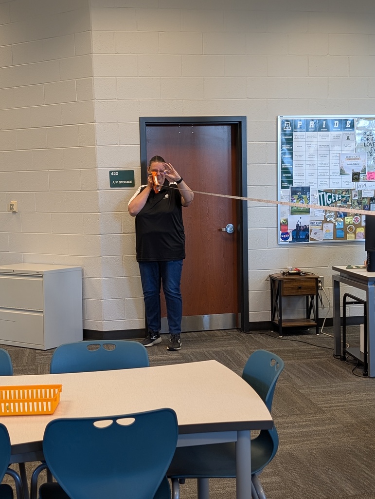 A teacher stands with a marble and tape measure as she tries to determine the distance at which the moon (a marble) blocks out the sun (a beach ball).