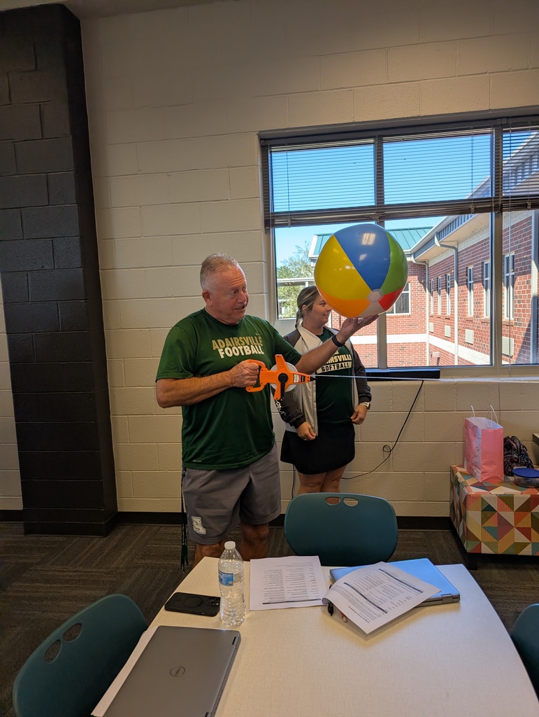 A teacher stands with a beach ball and tape measure as the group works to determine the distance at which the moon (a marble) blocks out the sun (a beach ball).
