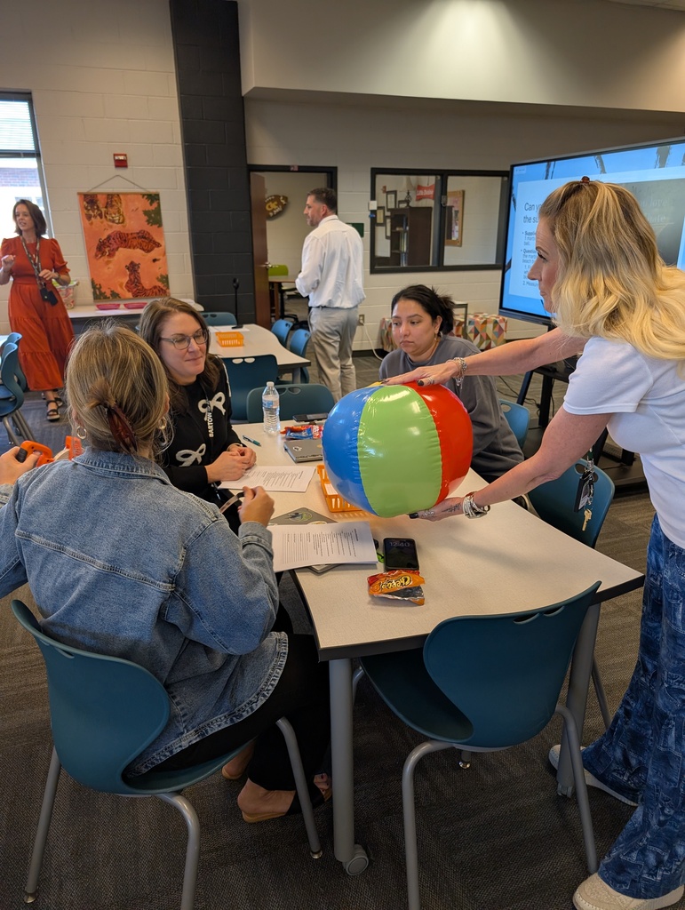 Teachers sit in a group as they work to determine the distance at which the moon (a marble) blocks out the sun (a beach ball).