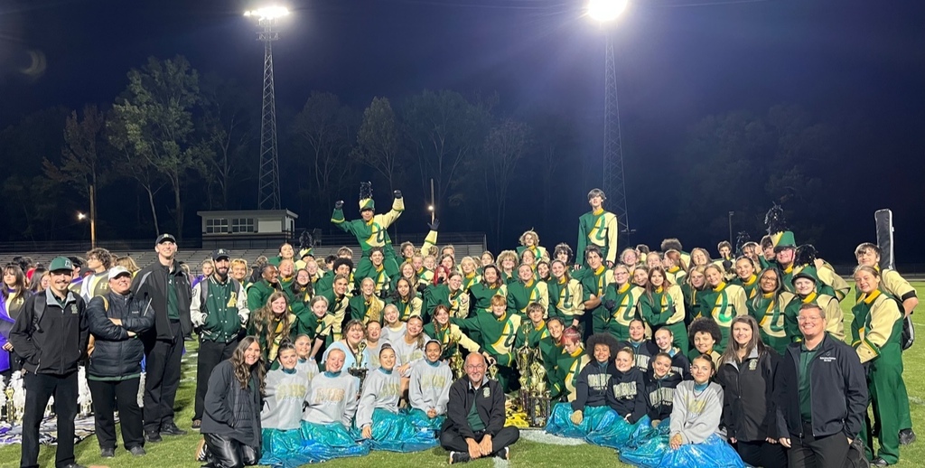 A large group of people in green and white uniforms standing and sitting on a field at night.