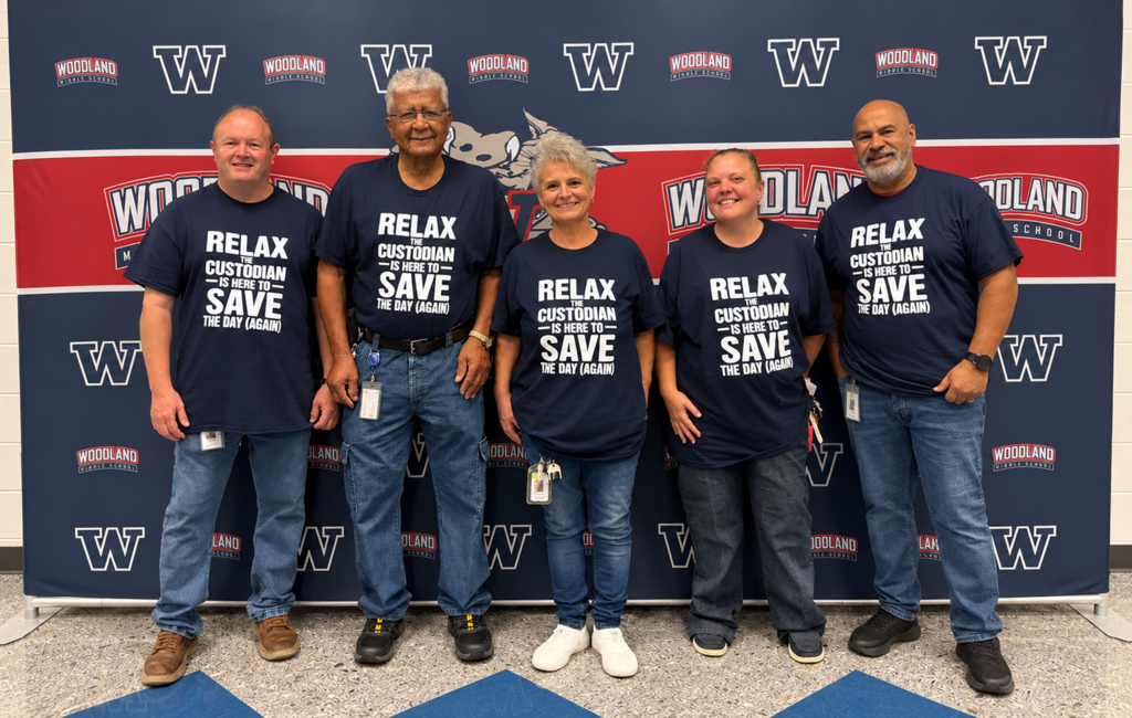 Five people pose in matching blue T-shirts with a message. They stand next to each other with a large blue wall behind them.