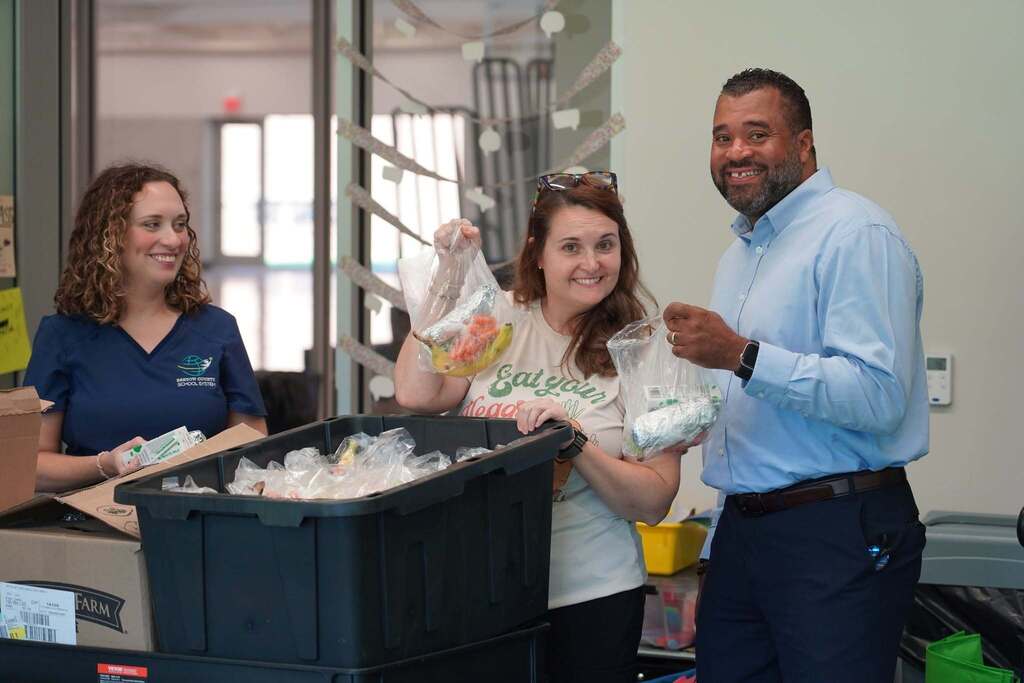 Three adults smiling with a large bin of food, a small bin, and bags of food.