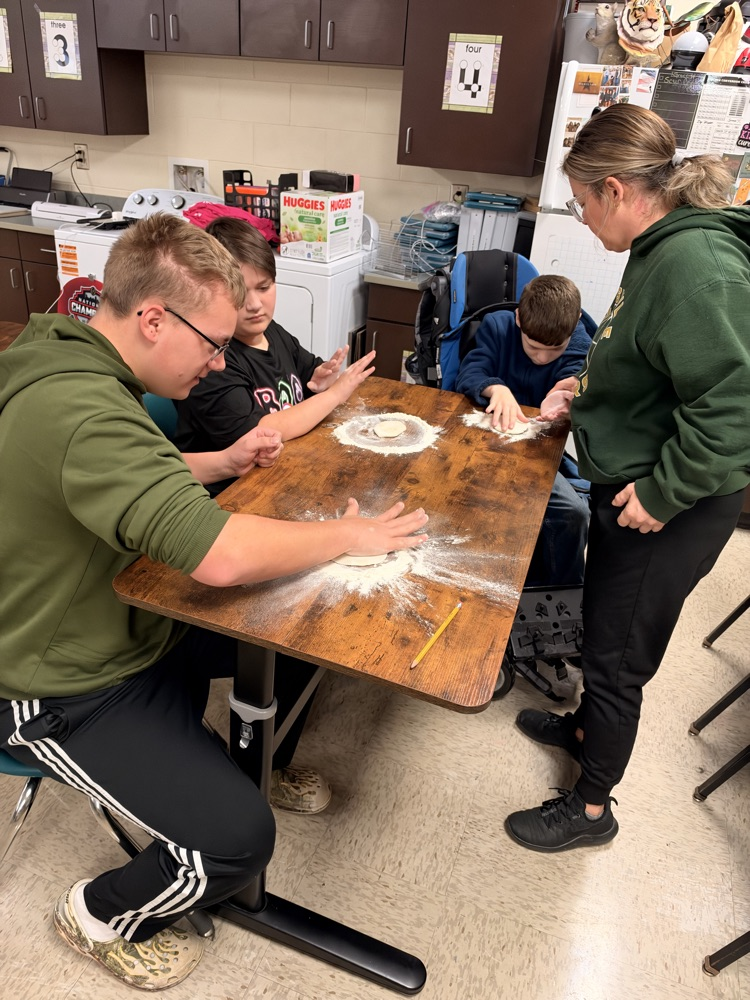Four students work on a table covered in flour. One person is seated in a wheelchair.