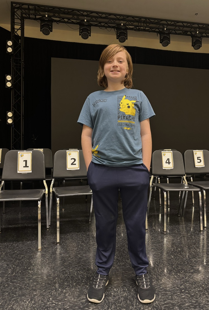 Child stands in front of rows of numbered chairs, in a room with a stage and a large screen.