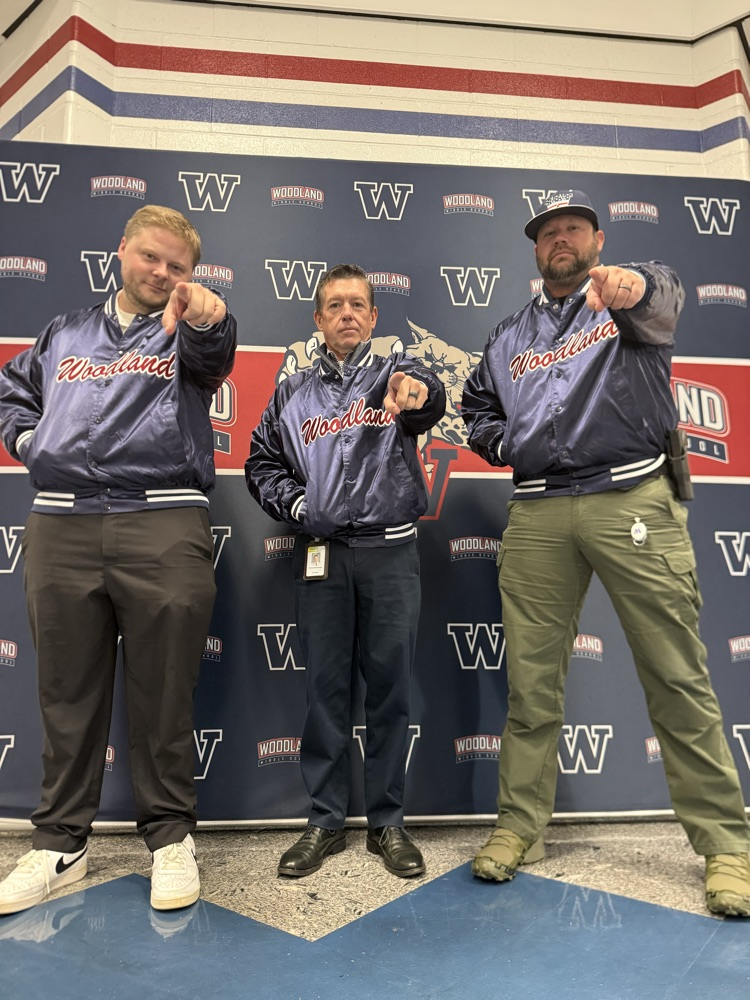 Three men in matching blue jackets standing in front of a wall with "W" and "ND" letters.