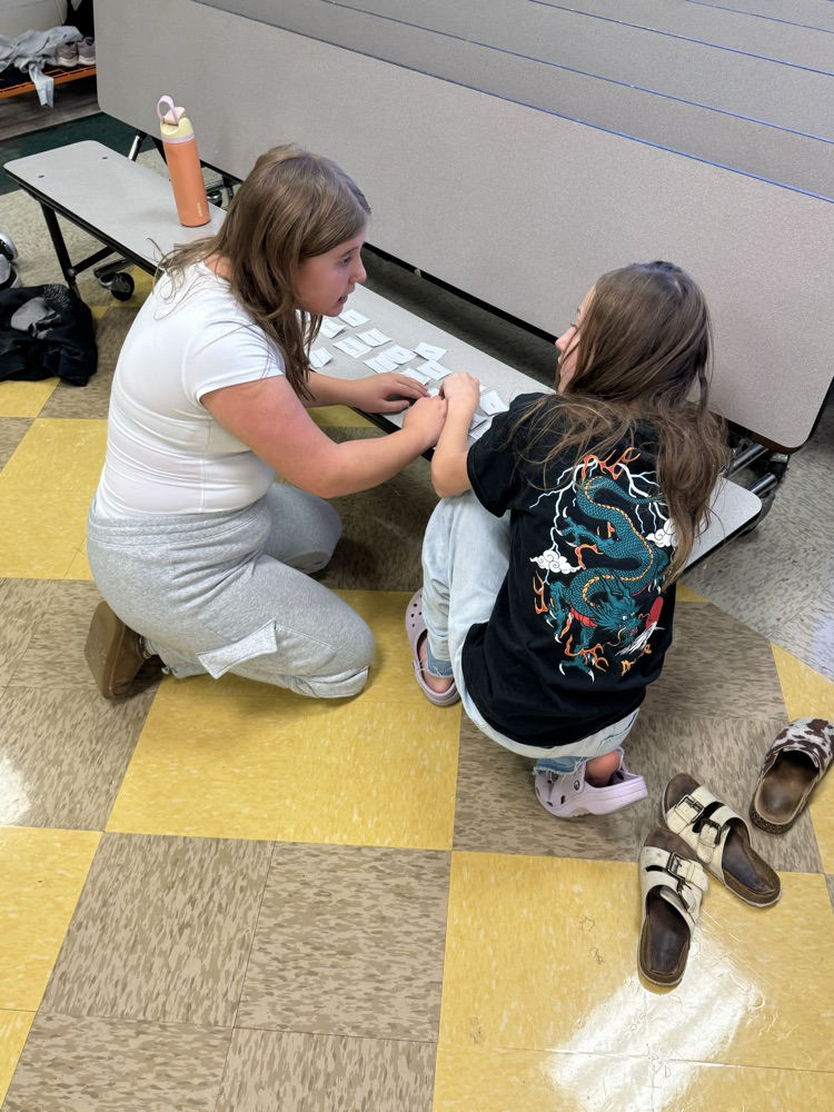 Two students kneeling on a floor, one typing on a keyboard while the other holds a mouse.