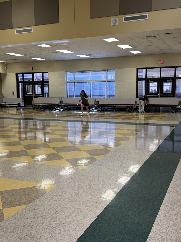Two people walking on a checkered floor, one person in sneakers, another in a white shirt.