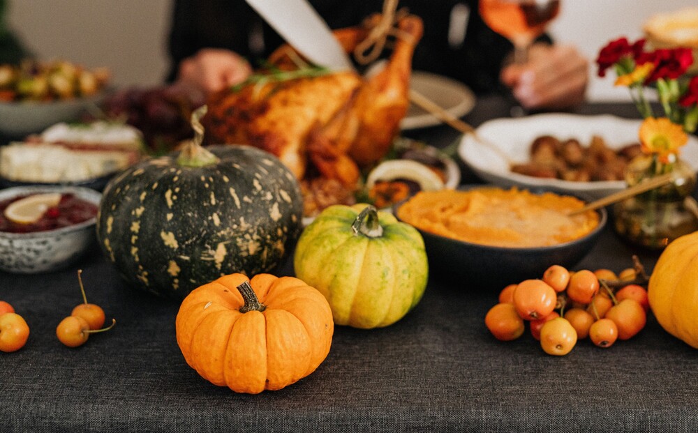 A table with gray table cloth and Thanksgivinng meal with decorative gourds around it