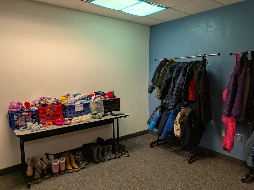 Jackets and snow pants hanging on rack and bins with hats and gloves on a table