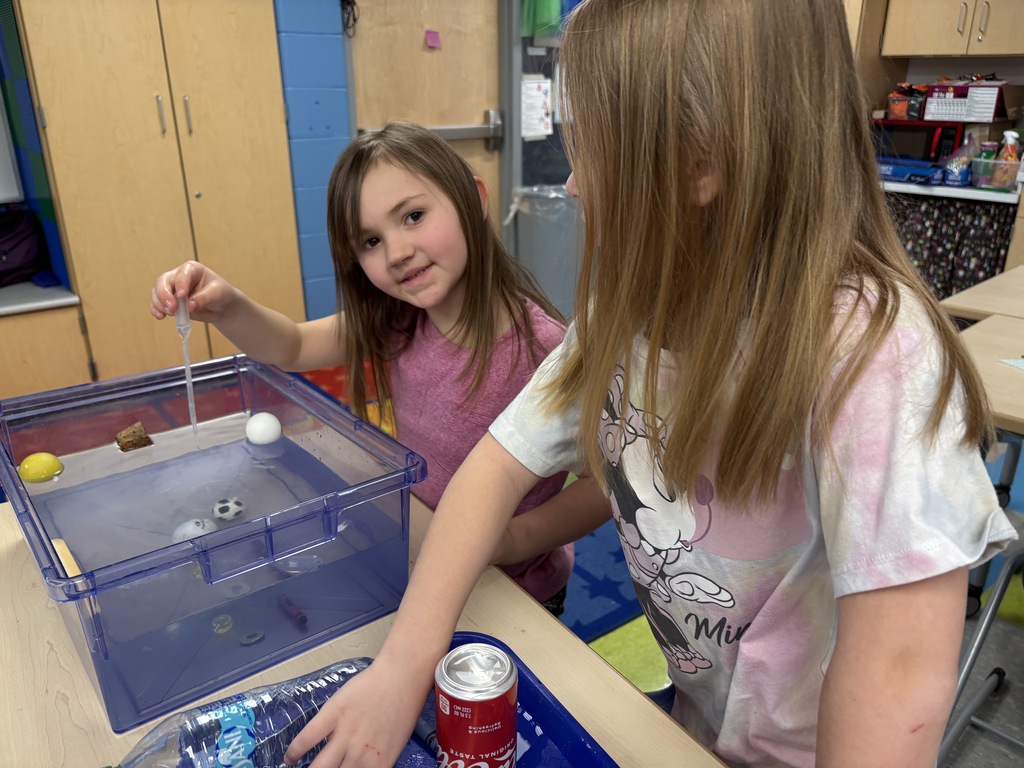 Girls standing in front of bin with water and objects