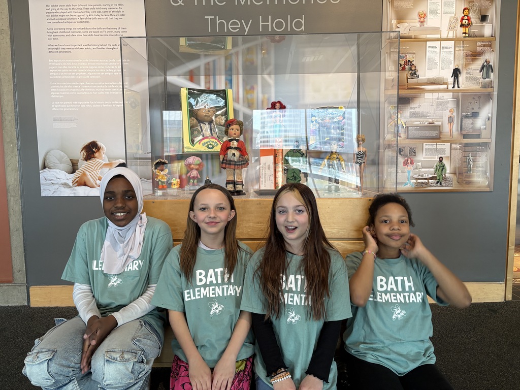 Girls sitting in front of a doll display