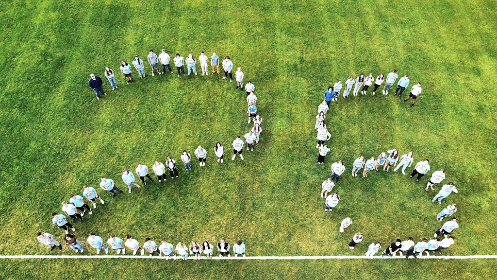 Senior class standing on the football field in the formation of the number 26