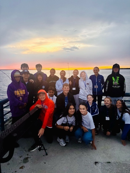 Students on a boat with fishing poles at sunrise.
