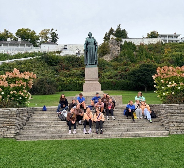 Students sitting for a photo in front of a statue.