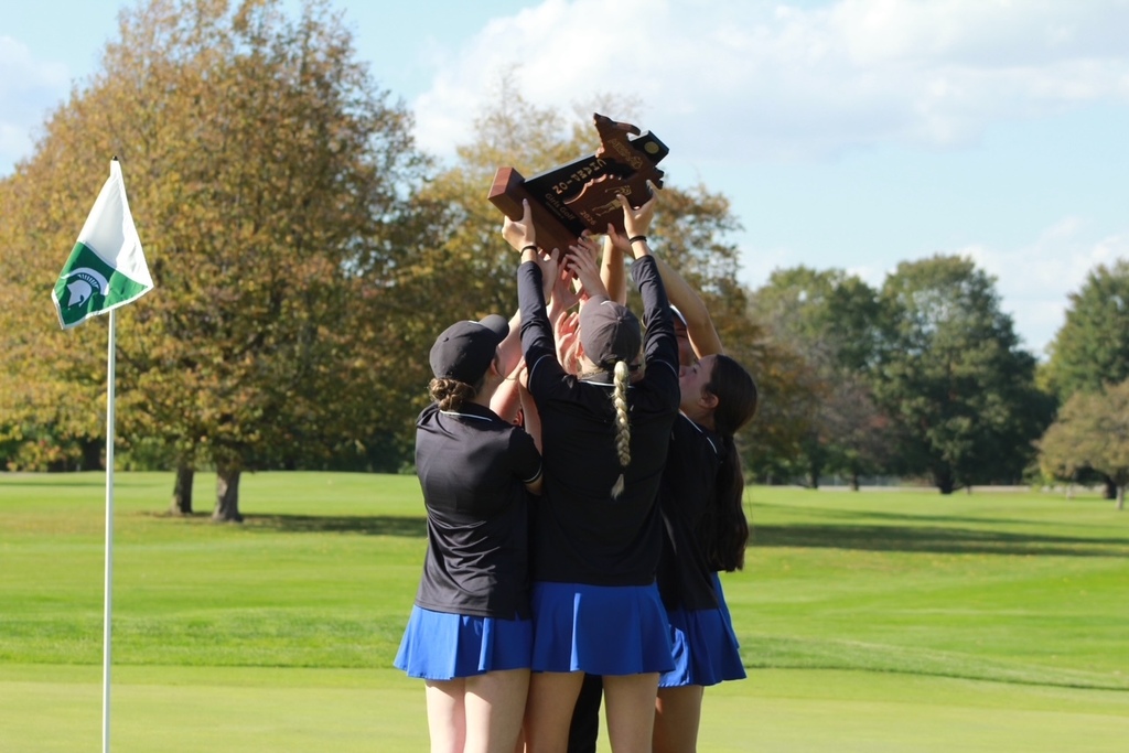 The girls team players standing in a circle facing each other holding the trophy above their heads