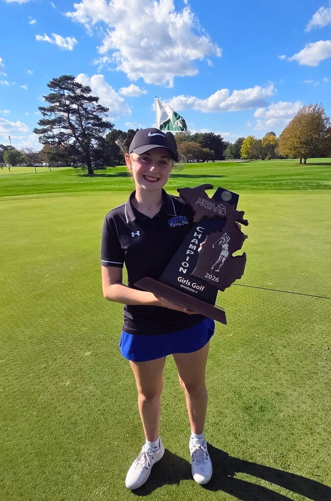 Addi standing on the grass wearing her golf uniform holding the trophy
