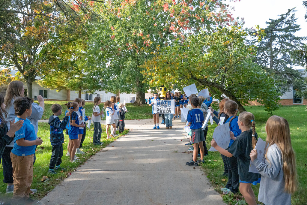 Elementary students lining the sidewalk holding sign to support high school athletic teams