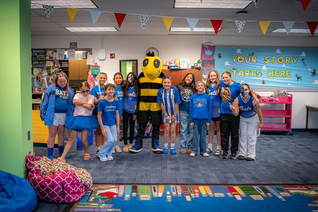 5th grade girls dressed in bath gear standing with the Bee mascot in the elementary library