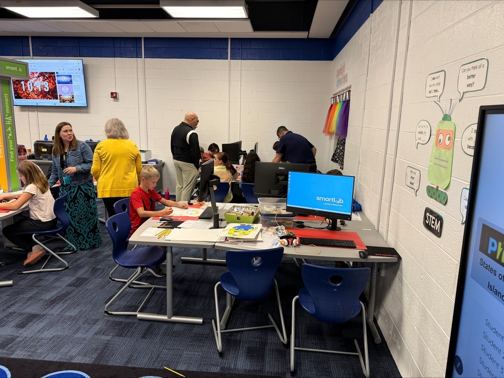 Adults standing behind studenst working at their desks