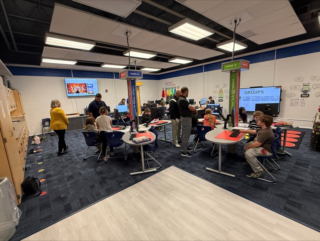 Students working at a tables while audlts stand around the room watching them work