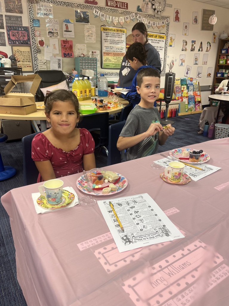 Boy and girl sitting at table with pink table cloth. Food on fancy plates is sitting on the table