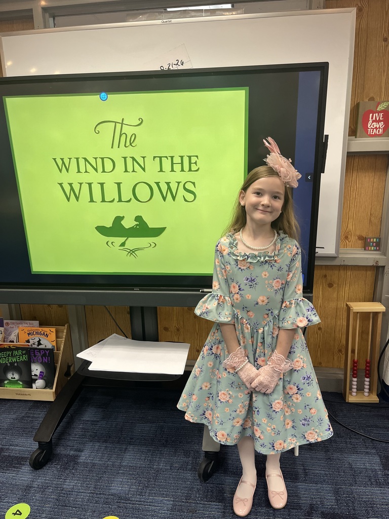 Girl in floral dress with pink hat standing in front of display that says The Wind in the Willows