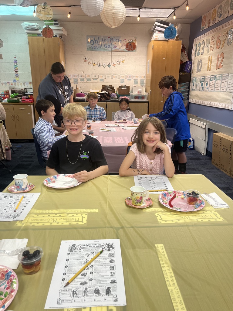 Girl and boy sitting at table with yellow table cloth eating food and doing a paper worksheet