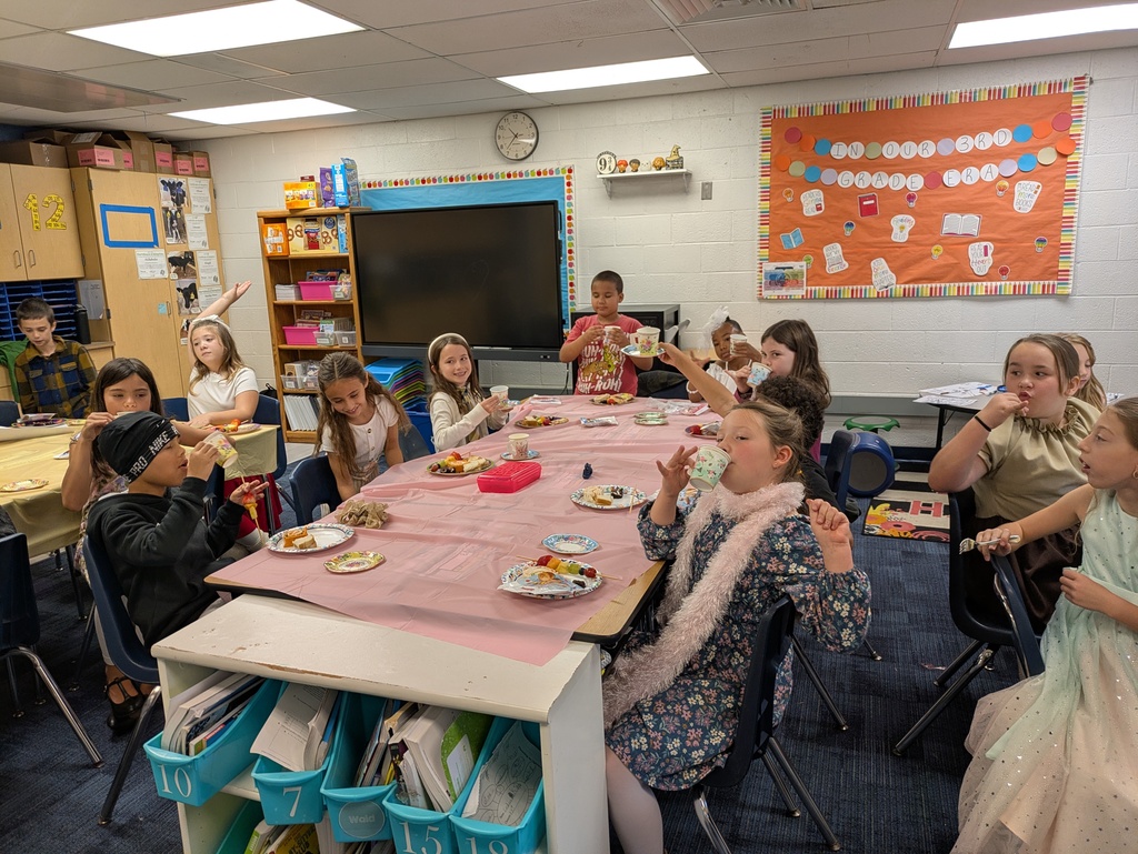 A group of students dressed up and sitting at a table with a pink table cloth having a tea party