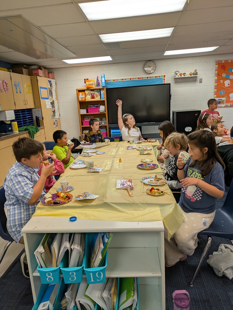 A group of students dressed up and sitting at a table with a yellow table cloth having a tea party