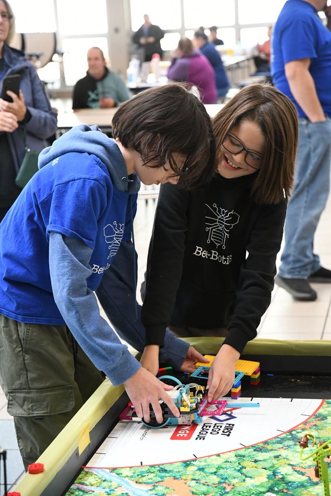 2 boys smiling and working on a robot at the table