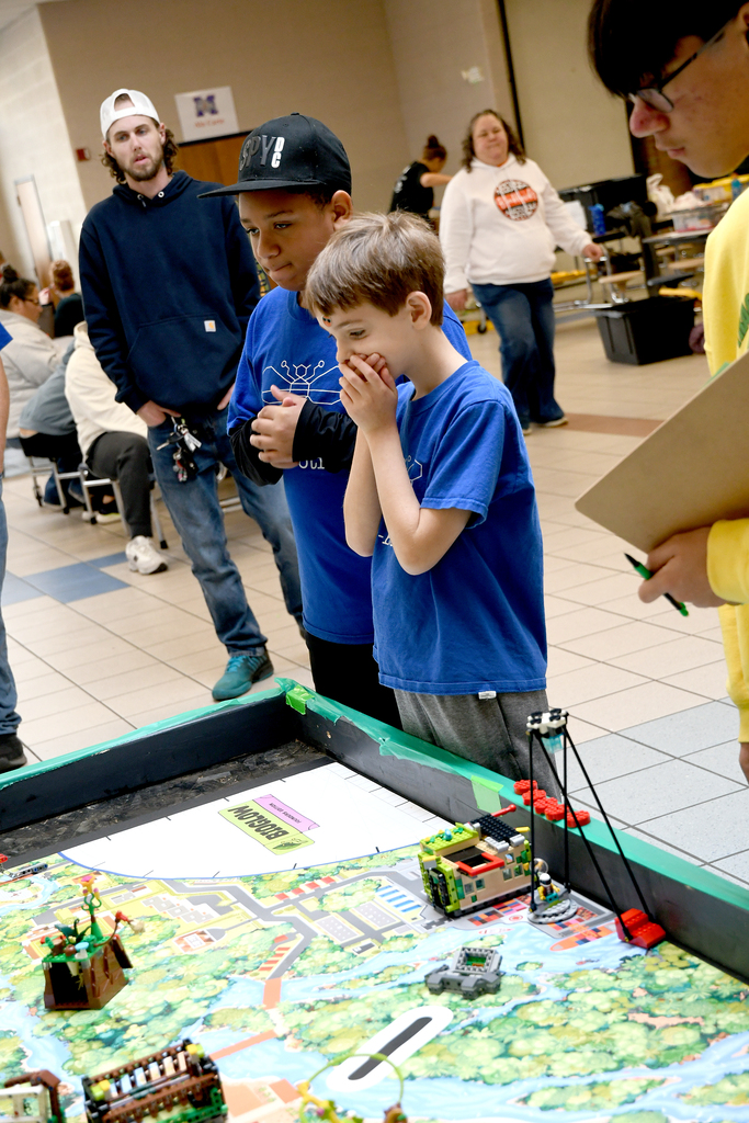Boys watching their robot on the table. One boy has his hands over his mouth
