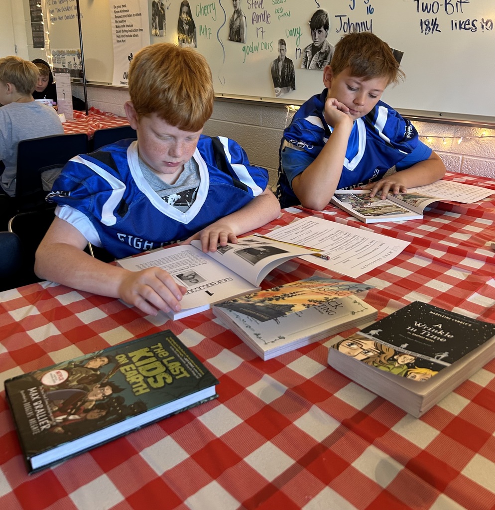 2 boys with blue and white football jerseys reading books.