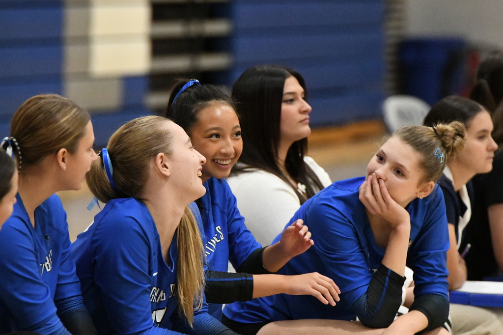Girls volleyball team members wearing blue jerseys sitting in chairs on the sideline