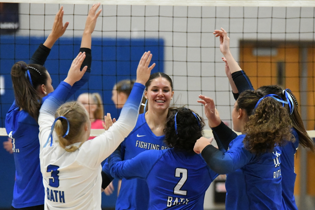 Volleyball players in blue and white jerseys with arms up celebrating in front of the net