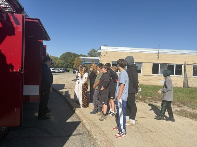 Students on a sidewalk in front of a red fire truck.