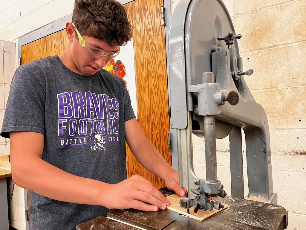 A student uses a bandsaw to cut their initials out of plywood.
