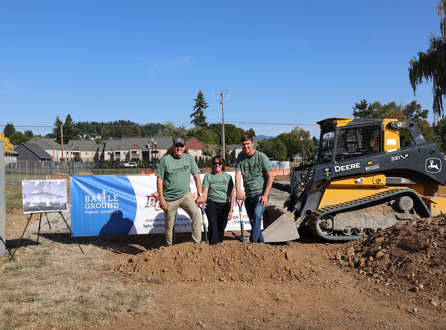 Three people stand near the site of the future construction trades building