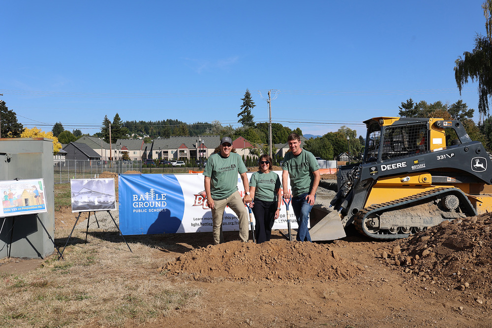 Three people stand near the site of the future construction trades building