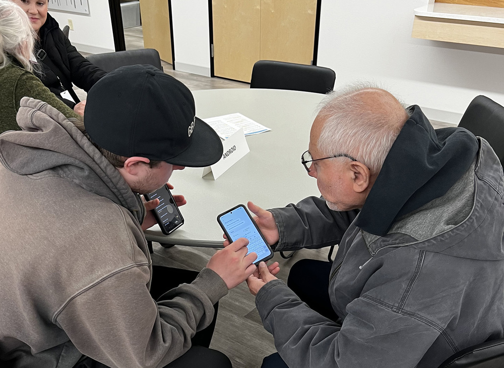 high schooler shows a man how to use his cell phone
