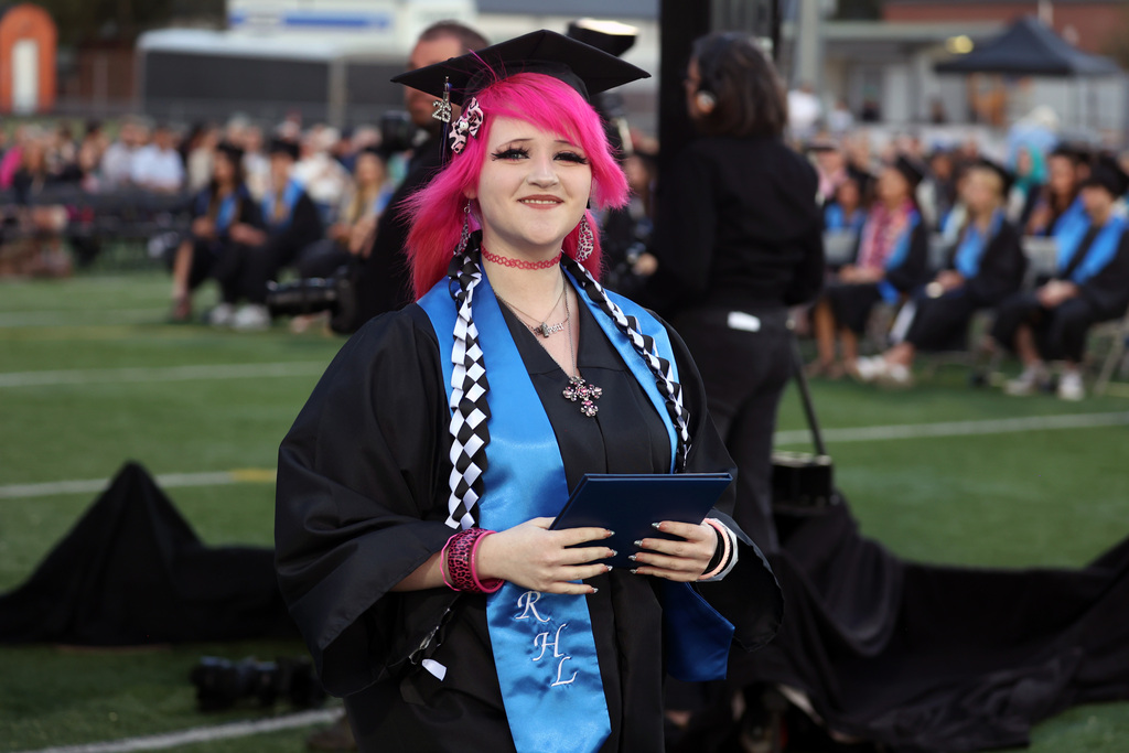 A grad beams while holding a diploma