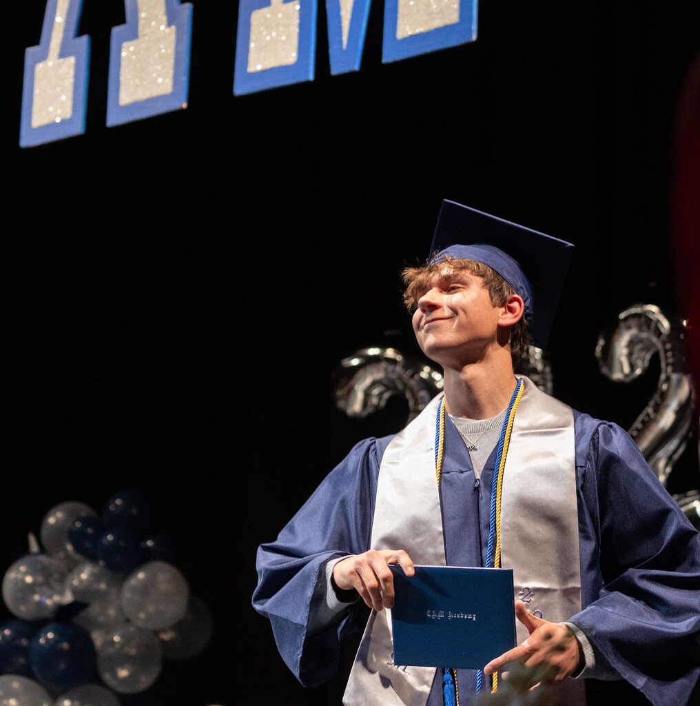 A proud young man holds up his diploma on the stage during graduation